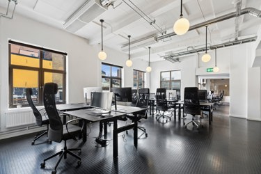 Lyst og romslig kontorlandskap med store vindusflater og flere arbeidsplasser.